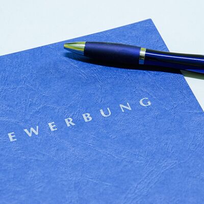 Eine blaue Bewerbungsmappe, auf der ein Kugelschreiber liegt.