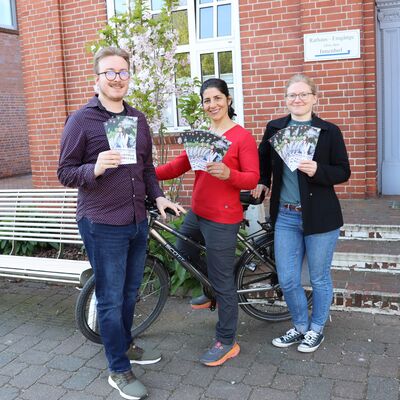 Radeln für das Klima: Rathausmitarbeiter Oliver Hahlbrock und die Klimamanagerinnen Sarah Zarin und Yasmin Eger halten die neuen Flyer in der Hand.